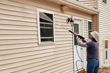 About People Helping People technician washing siding near windows